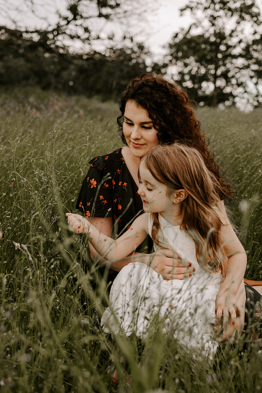 mother and daughter smelling flowers in field